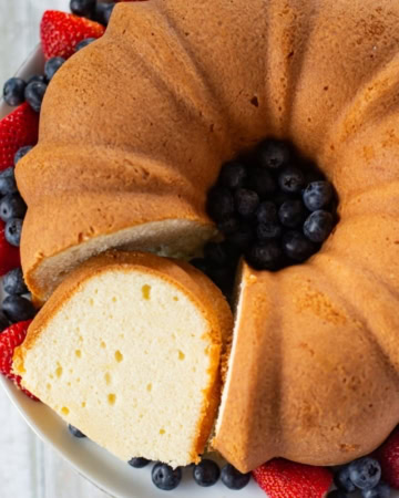A Pound Cake with a slice cut out served on a cake plate with fresh strawberries and blueberries encircling the cake.