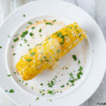 A sweet and tender ear of corn on the cob with a pat of melted butter, seasonings and fresh parsley from the How To Make Instant Pot Corn On The Cob