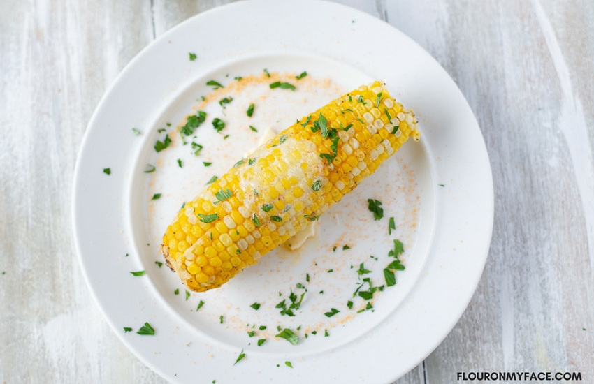 A sweet and tender ear of corn on the cob with a pat of melted butter, seasonings and fresh parsley from the How To Make Instant Pot Corn On The Cob