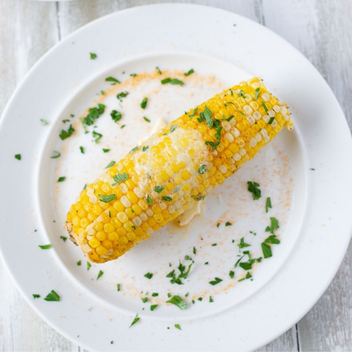 An ear of Instant Pot corn on the cob on a white plate, melted butter and parsley.