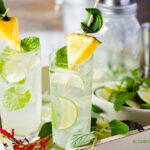 Pineapple Sage Mojito recipe in a tall glass on a serving platter with cocktail shaker and ingredients