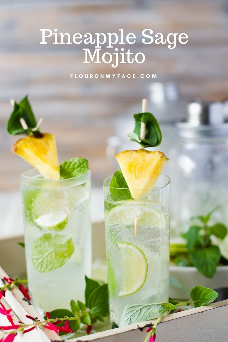 Tall glasses filled with Pineapple Sage Mojito cocktail on a serving tray with fresh pineapple and fresh mint.