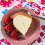 A slice of Million Dollar Pound Cake on a dessert plate served with fresh strawberries and blueberries.