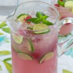 Tall glass pitcher filled with pink lemonade and fruit.