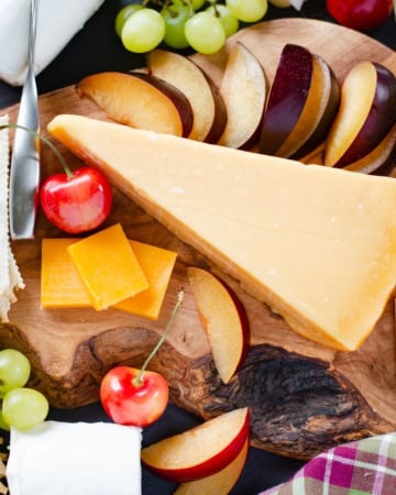 Cheese, fruit, nuts and crackers for a Cheese platter on a cutting board.