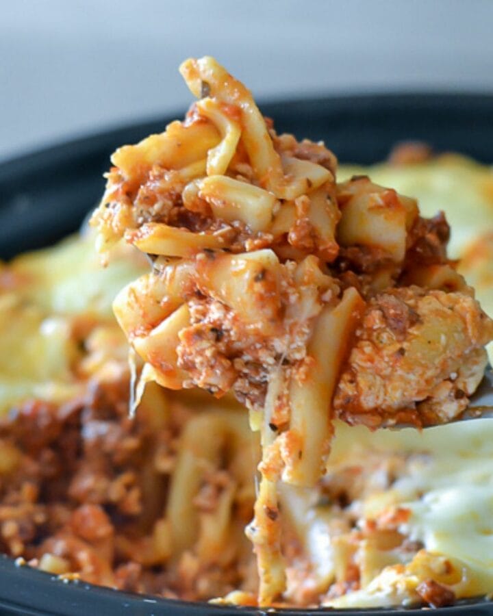 Closeup image of a serving spoon lifting crock pot baked ziti from the slow cooker.