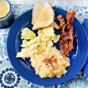 Serving cheesy hash brown breakfast potatoes with eggs, bacon and toast on a blue dinner plate.