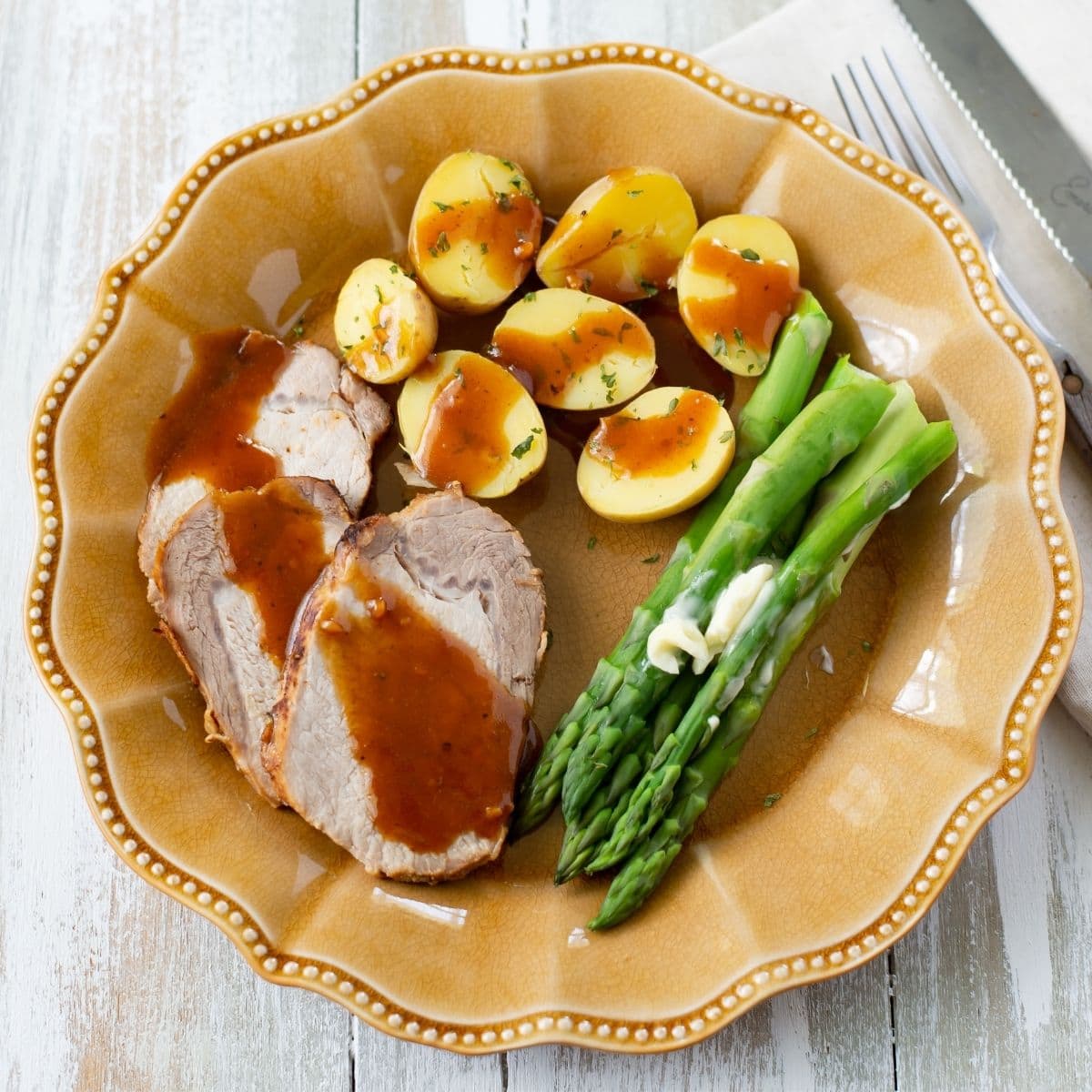 Honey garlic pork loin served on a dinner plate with potatoes and asparagus.