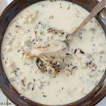 A brown and blue serving bowl of Creamy Crock Pot Wild Rice Soup recipe.