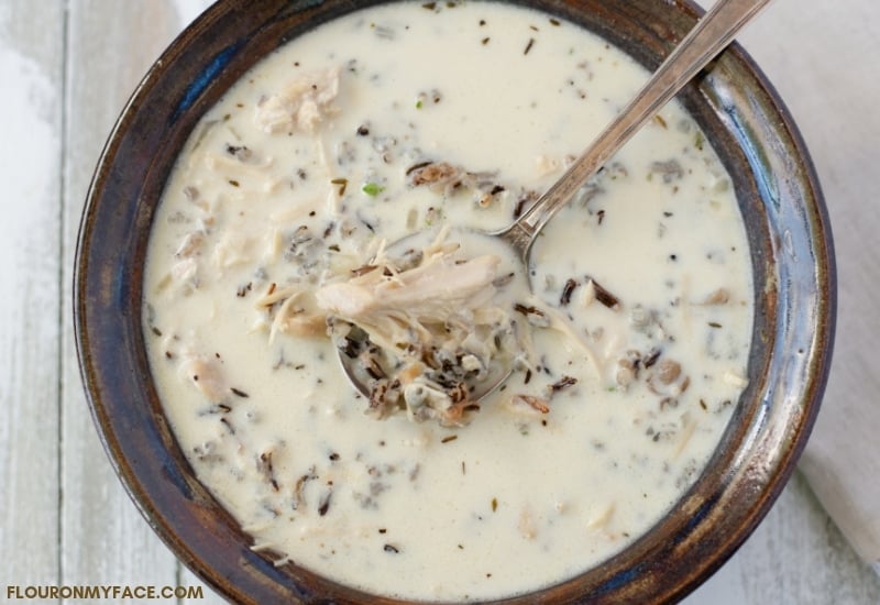 A brown and blue serving bowl of Creamy Crock Pot Wild Rice Soup recipe.