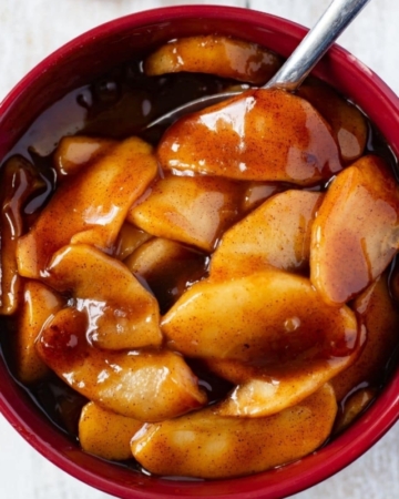 A brown bowl filled with Instant Pot Cinnamon Apples and a sliced pound cake on a wooden cutting board.