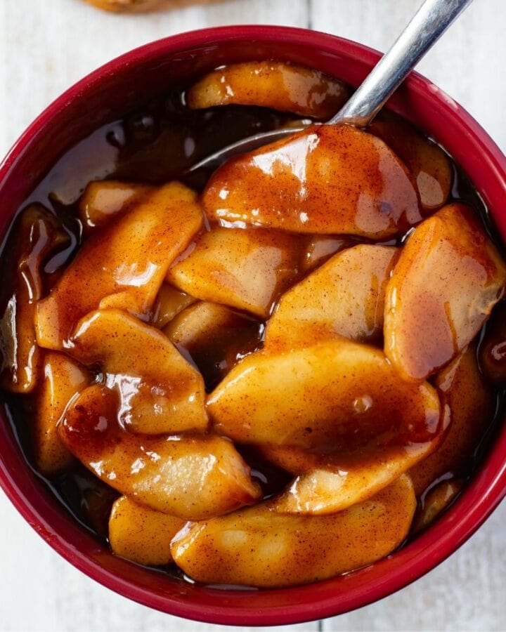 A brown bowl filled with Instant Pot Cinnamon Apples and a sliced pound cake on a wooden cutting board.