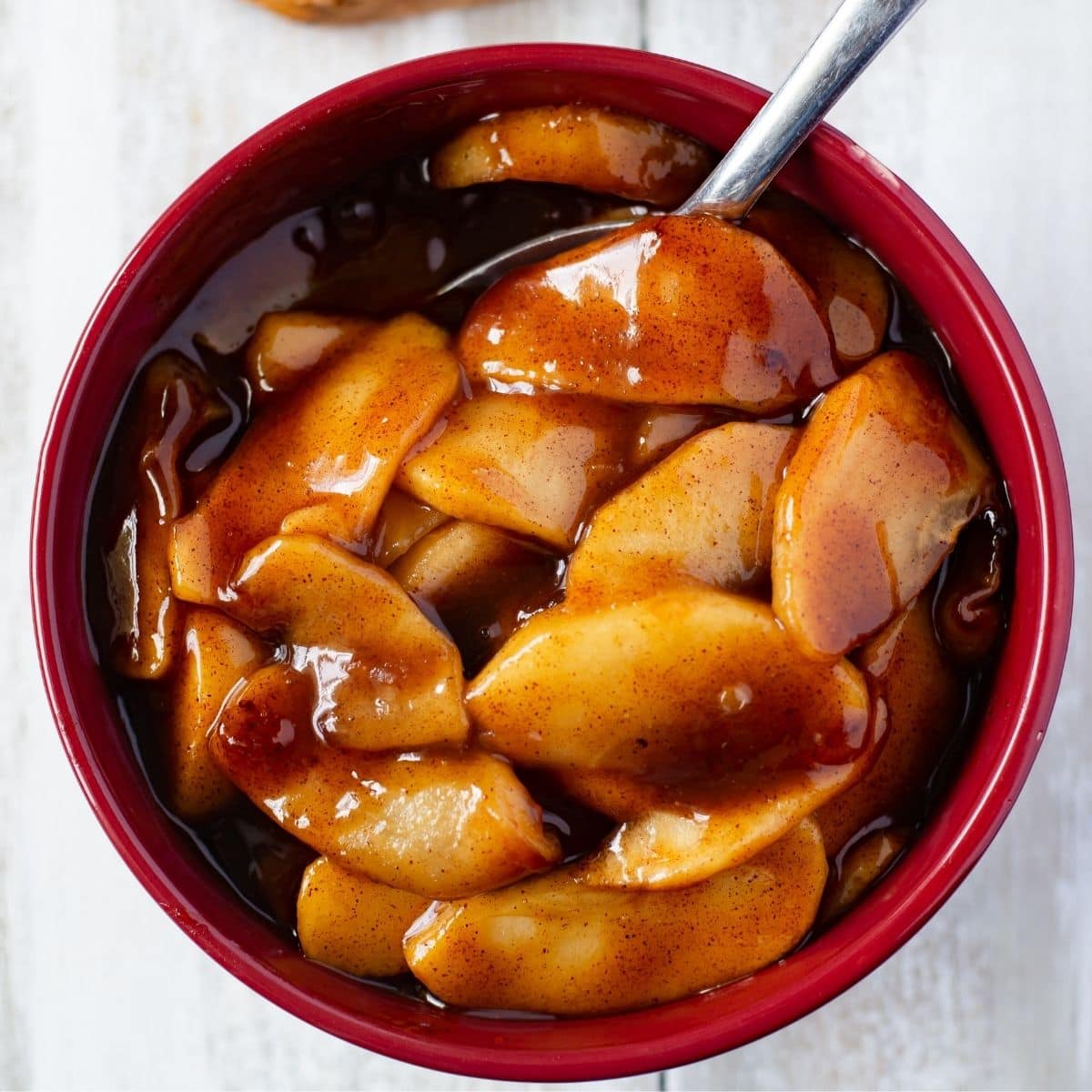 A brown bowl filled with Instant Pot Cinnamon Apples and a sliced pound cake on a wooden cutting board.