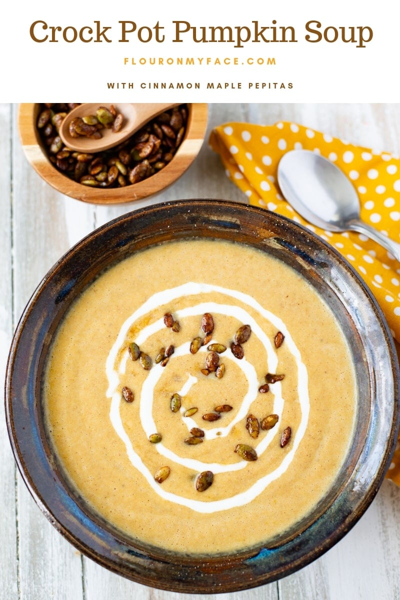 Crock Pot Pumpkin soup in a brown bowl, yellow napkin, spoon and small bowl of cinnamon maple toasted pumpkin seeds