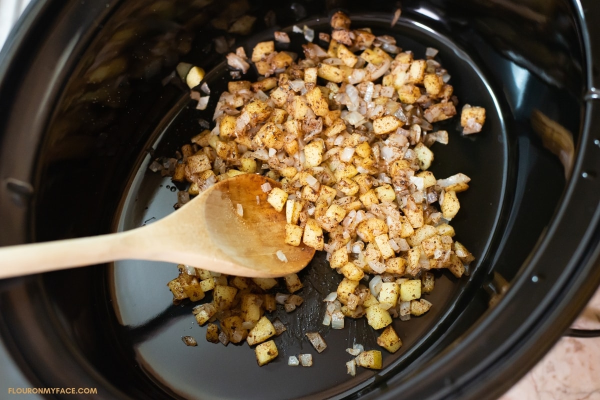 sautéed diced apples, onions, and spices inside a crock pot with a wooden spoon