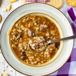 A bowl of Instant Pot Beef Barley Soup with a purple and white cloth napkin and Ritz crackers
