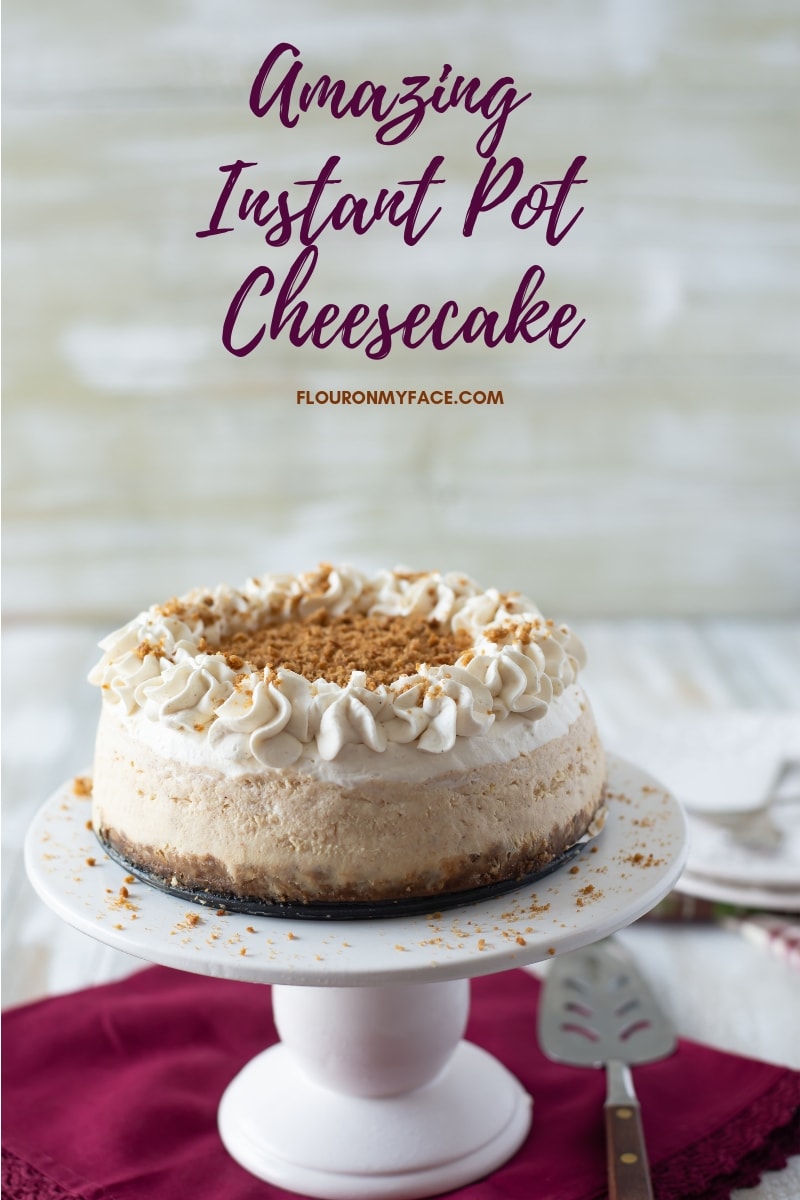 Instant Pot Eggnog Cheesecake on a glass cake stand with a mauve cloth napkin, dessert plates, and dessert forks.