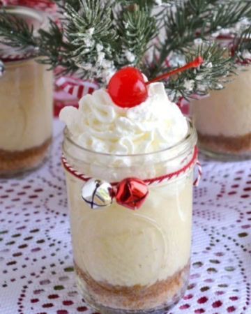 Holiday eggnog cheesecakes in mason jars served with whipped cream and topped with a cherry.