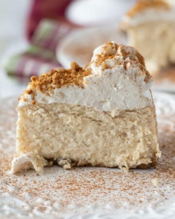 Eggnog cheesecake topped with whipped cream and dusted with cinnamon on a plate.