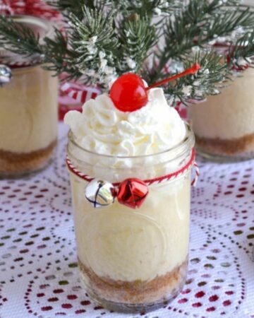 Holiday eggnog cheesecakes in mason jars served with whipped cream and topped with a cherry.