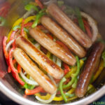 How To Make Instant Pot Brats photo with browned brats and sliced peppers and onions inside the Instant Pot