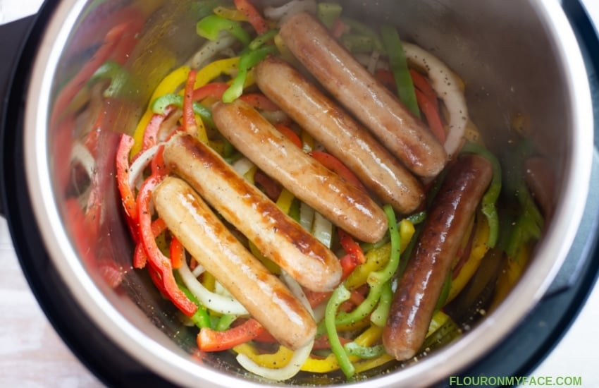How To Make Instant Pot Brats photo with browned brats and sliced peppers and onions inside the Instant Pot