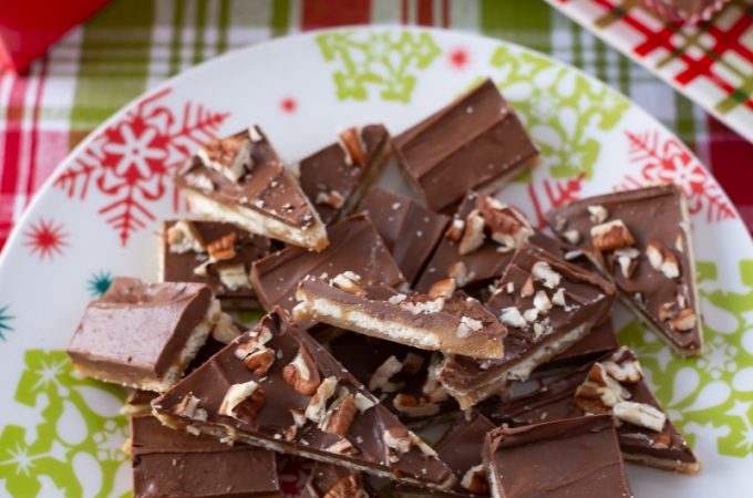 Saltine Cracker Toffee recipe cut into bite size pieces on a red and green Christmas serving plate.