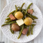 Instant Pot fresh Green Beans and new potatoes cooked with ham and served on a white plate with a pat of melting butter.