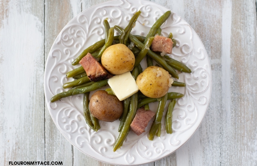 Instant Pot fresh Green Beans and new potatoes cooked with ham and served on a white plate with a pat of melting butter.