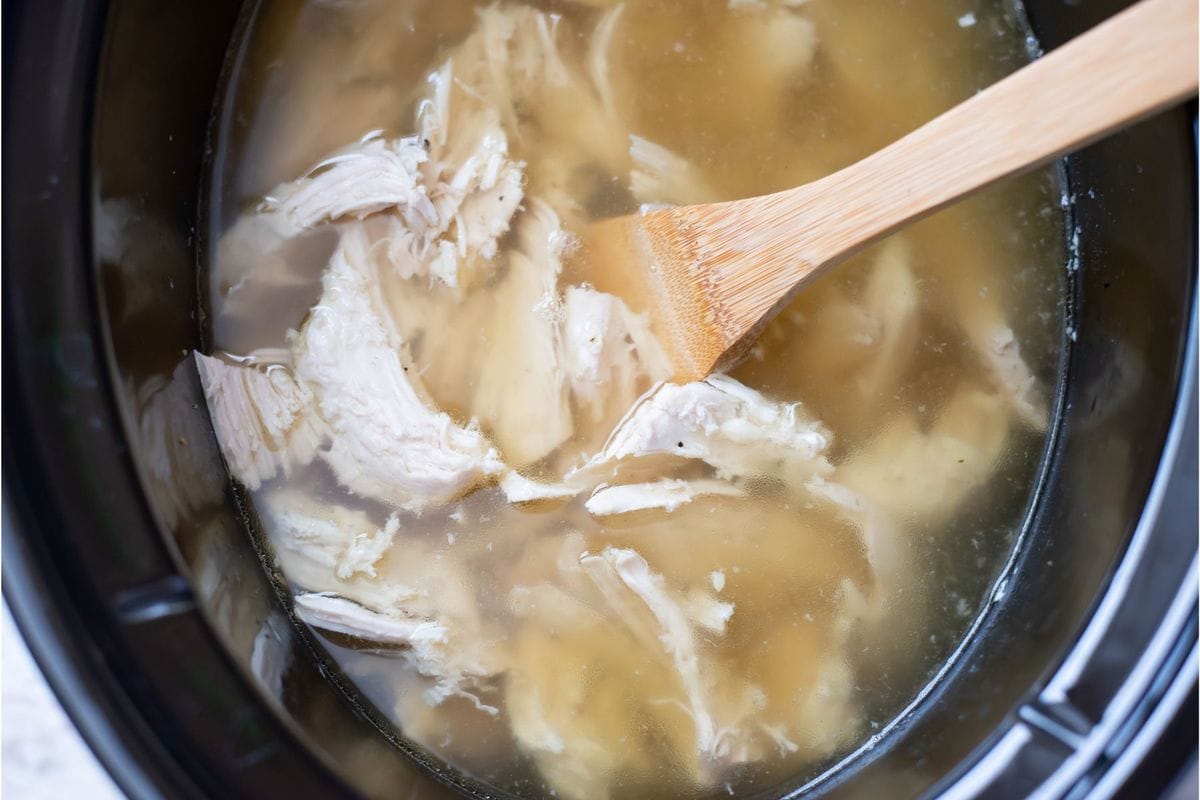 Shredded chicken in chicken broth in a slow cooker.