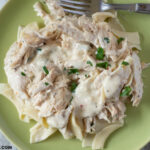 Crock Pot Cream Cheese Chicken recipe served over noodles on a green plate with a fork.