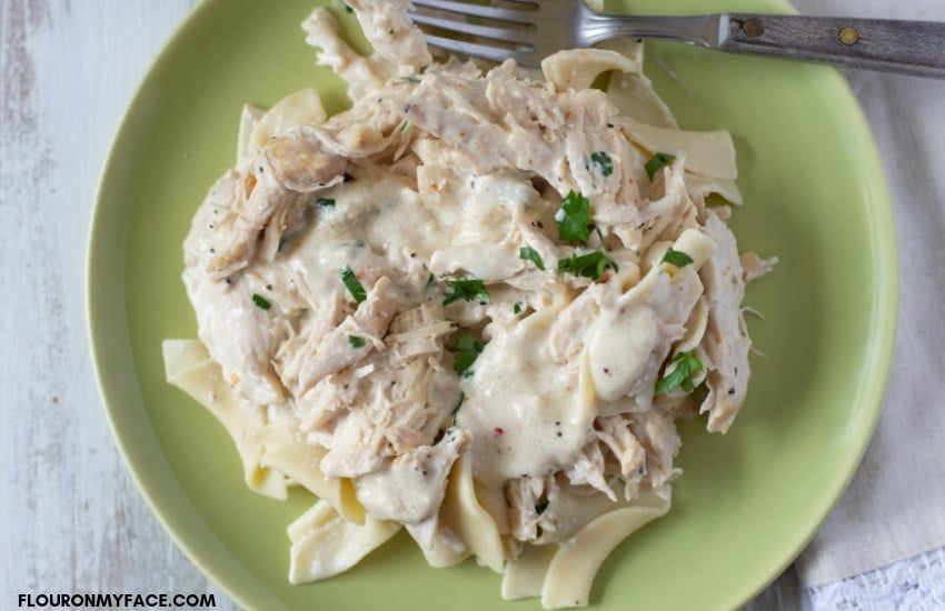 Crock Pot Cream Cheese Chicken recipe served over noodles on a green plate with a fork.