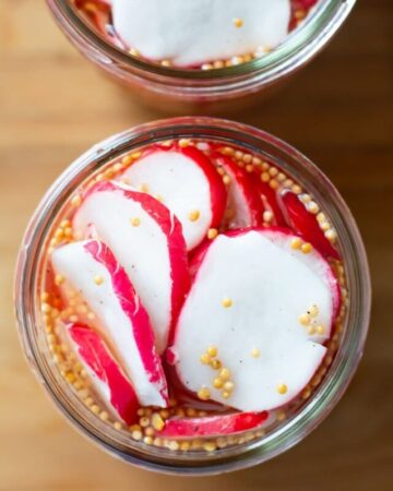 Overhead of an open canning jar filled with sliced radishes and spices.