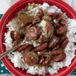 Red Fiestaware bowl with filled with Instant Pot Red Beans and Rice, served with crusty French bread