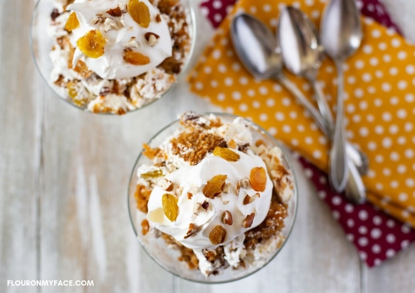 Carrot Cake Cheesecake Trifle served in glass dessert dishes topped with whipped cream, nuts, and golden raisins.