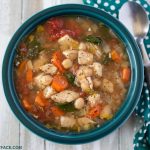 A teal bowl filled with Crock Pot Chicken Garbanzo Bean Soup served with saltine crackers