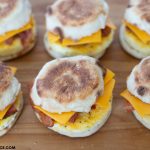 Image of 6 Freezer Breakfast Sandwiches on a wooden cutting board, ready to wrap in plastic wrap and put in the freezer.