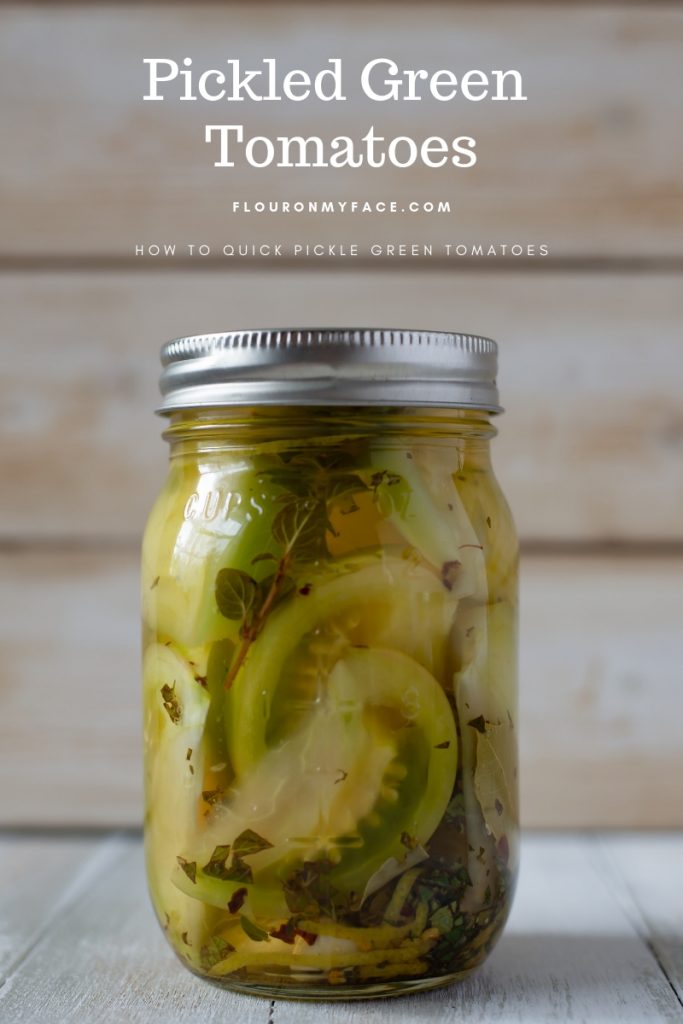 Canning jar full of pickled green tomatoes with herbs, spices and fresh garlic cloves