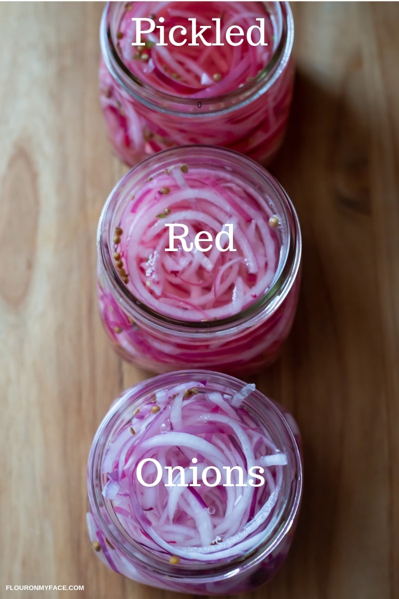 Three glass jars lined up vertically, filled with sliced red onions and a pickling brine.