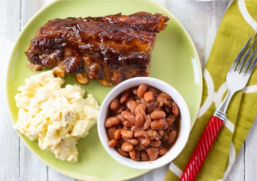 Instant Pot Barbecue Ribs recipe served with baked beans and homemade potato salad on a green plate with a green cloth napkin