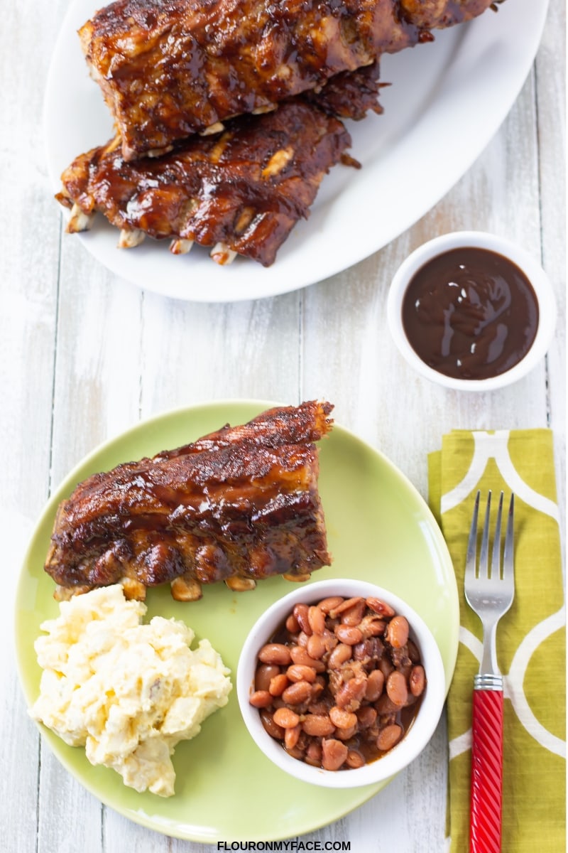 serving Instant Pot Ribs slathered in barbecue sauce with a small bowl of baked beans and a serving of potato salad