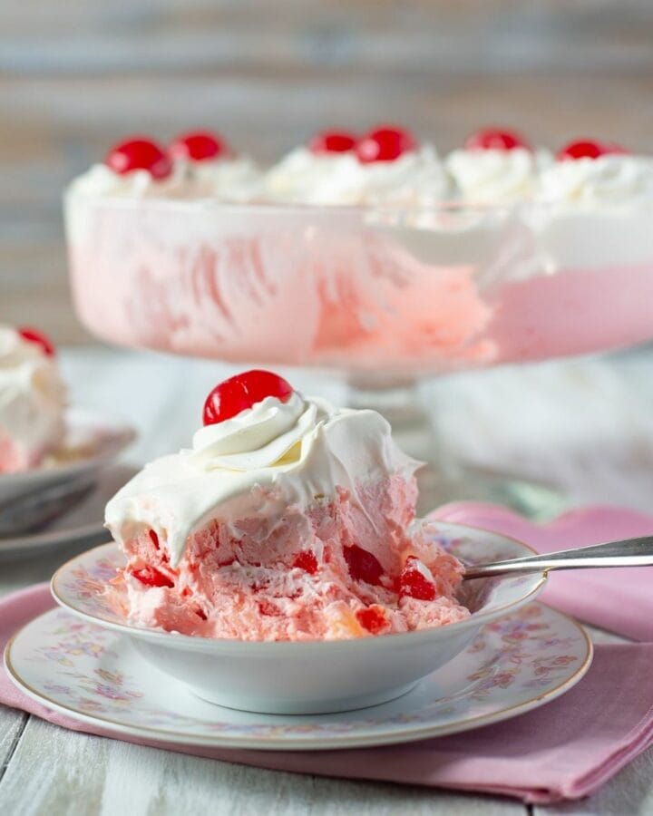 Pink Dessert Salad topped with whipped cream and a cherry in a bowl.