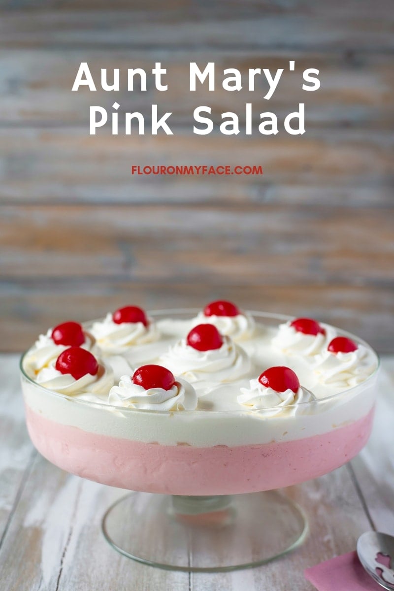a trifle bowl filled with the pink and white layers of Pink Salad, Cool Whip and maraschino cherries.