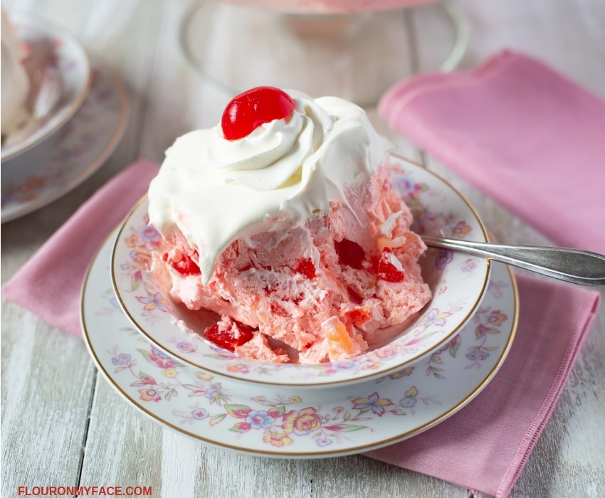 Pink Salad recipe made with maraschino cherries topped with Cool Whip and served on a vintage floral dessert dish.