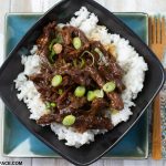 A black glass bowl filled with a serving of crock pot Mongolian Beef served over cooked white rice.