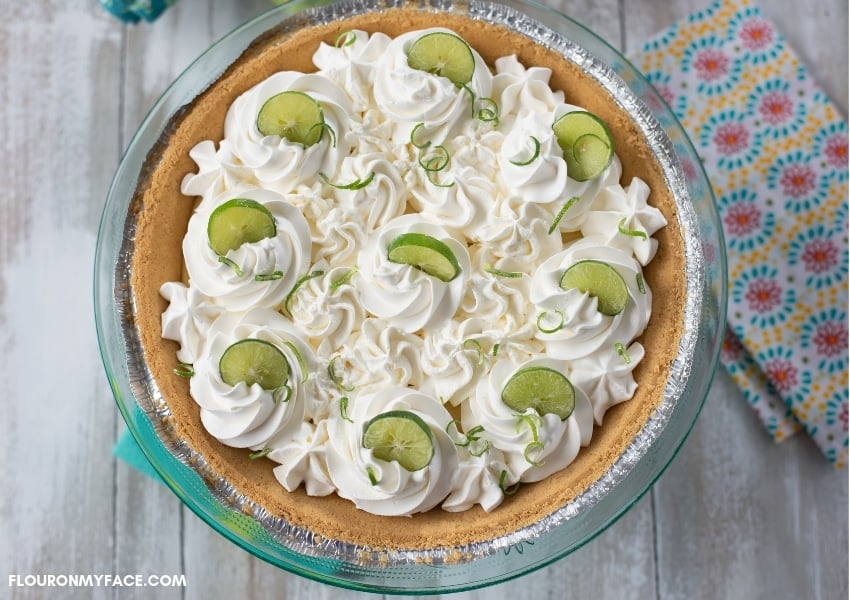 An uncut Key Lime Pie topped with whipped cream rosettes and garnished with Key lime slices