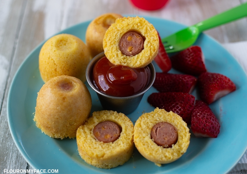 A blue plate with Instant Pot Corn Dog Bites and fresh sliced strawberries.
