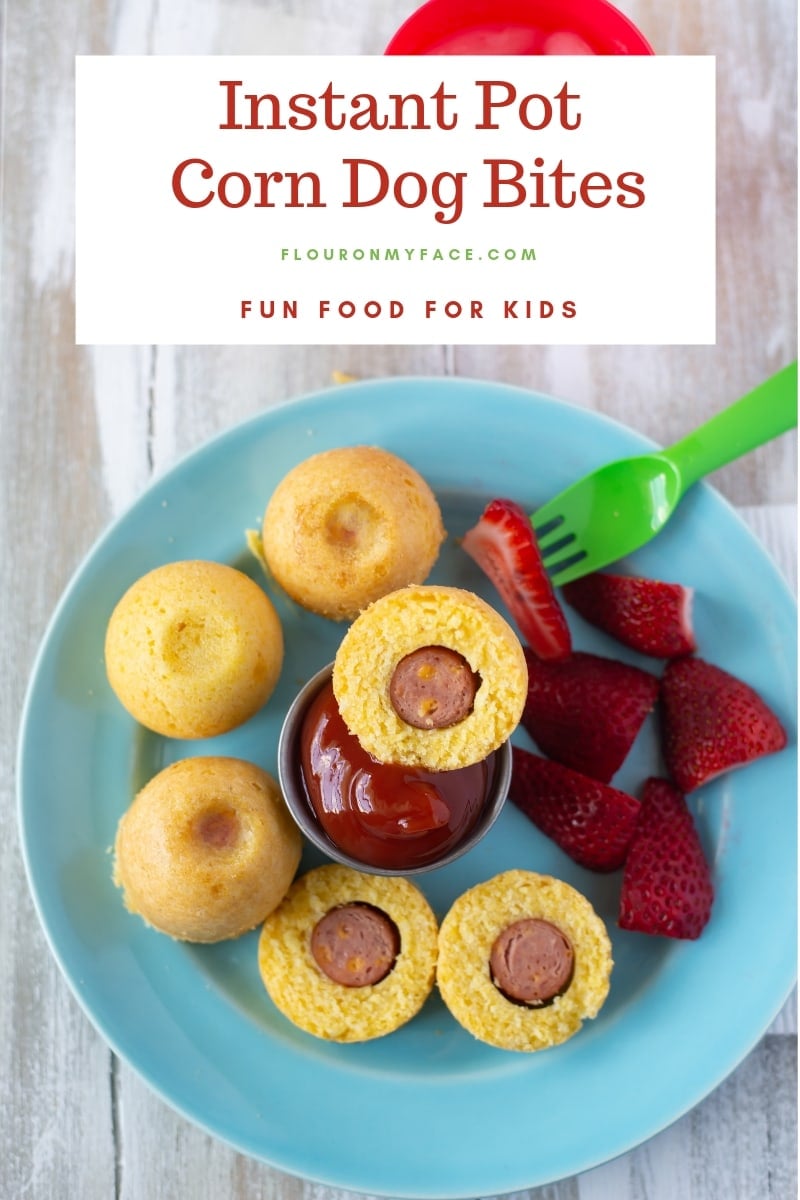 Instant Pot Corn Dog Bites served on a teal glass plate with a cup of ketchup and sliced strawberries for a summer time lunch.