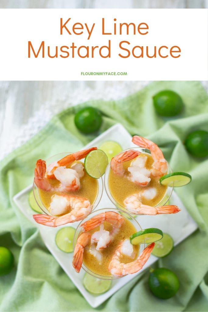 3 mini plastic martini appetizer glasses filled with Key Lime Mustard Sauce and boiled pink shrimp on a green cloth napkin with fresh key limes