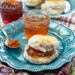 A plate with a fresh biscuit with a thick spread of homemade Scuppernong Jelly with a jar of the jelly on a cloth napkin.